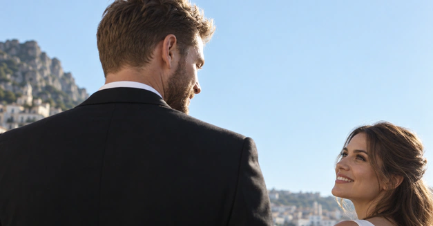 Groom seen from behind, looking at his bride with a coastal town beyond